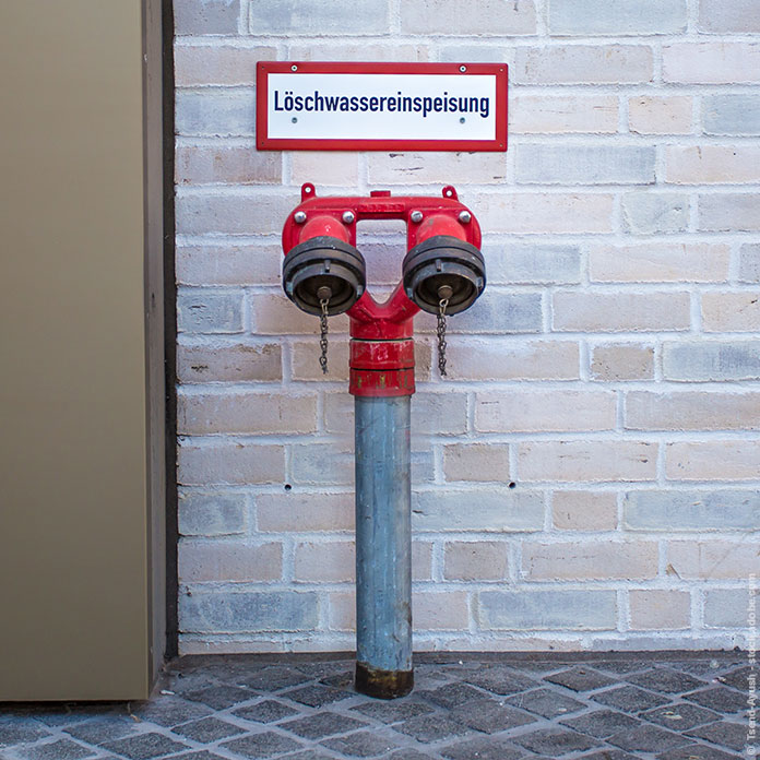 An einem Gebäude befindet sich eine Löschwasserversorgung mit zwei Auslässen.