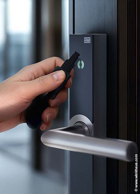 Eine Hand hält einen elektronischen Schlüssel an Winkhaus Schließanlage